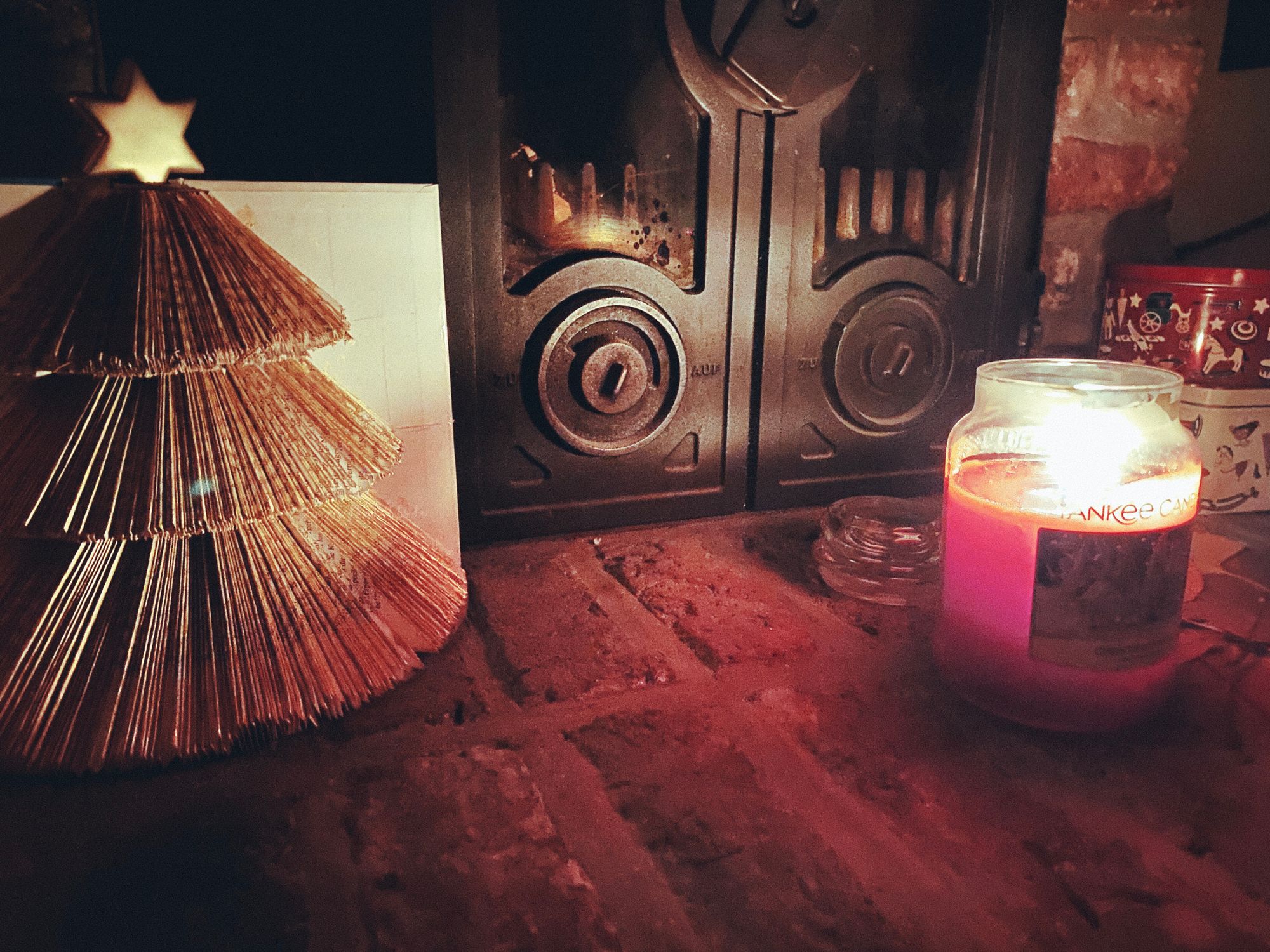 Links im Bild: Papiertannenbaum. Rechts brennt eine Kerze in einem Glas. Im Hintergrund: Plätzchendosen und ein Kamin.