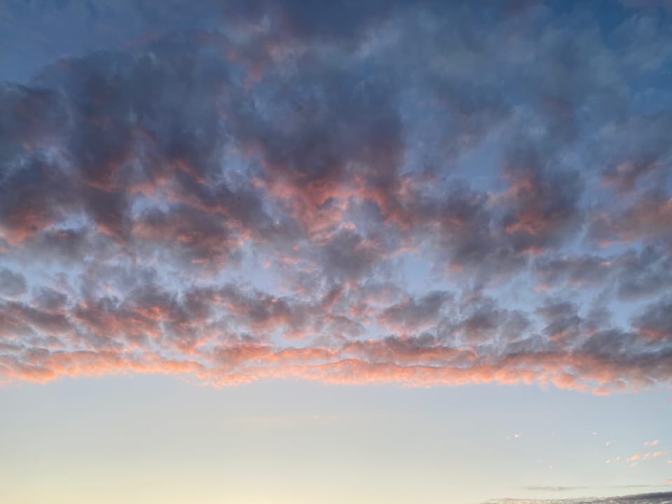 in der unteren Hälfte ist hellblauer Himmel, dadrüber Wolken, die von der Sonne rosa leuchten